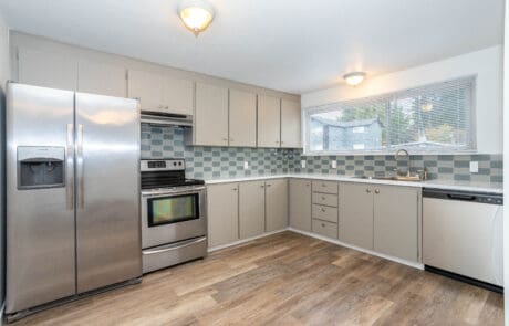 Apartments for Rent in Shoreline, WA - Octavia - L-Shaped Kitchen with Silver Appliances, Wood Floors, Grey Cabinetry, Blue Tile Backsplash, and Nearby Window